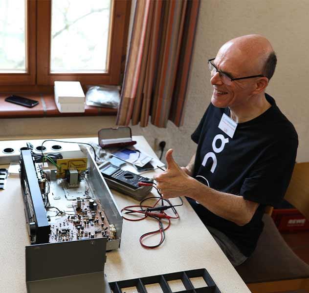 mitmacherei-team-team-klima_2 Ein Team-Mitglied der mitmacherei sitzt vor einem geöffneten elektrischen Gerät und streckt den Daumen nach oben