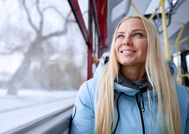 Frau sitzt am Fenster im Bus und schaut auf verschneite Landschaft draußen © Adobestock – serhiibobyk