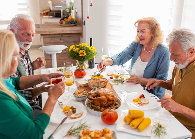 Vier Senioren sitzen an einem gedeckten Tisch und essen Hühnchen und verschiedenes Gemüse © Adobestock –  Impact Photography 