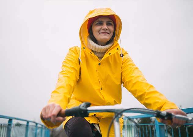 Lächelnde Frau auf einem Fahrrad mit gelbem Regenmantel © Adobestock – yossarian6